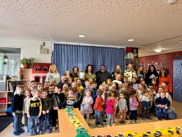 Auf dem Gruppenbild sind viele kleine Kinder in einem Kindergarten zu sehen. Dabei sind 10 Erwachsene.