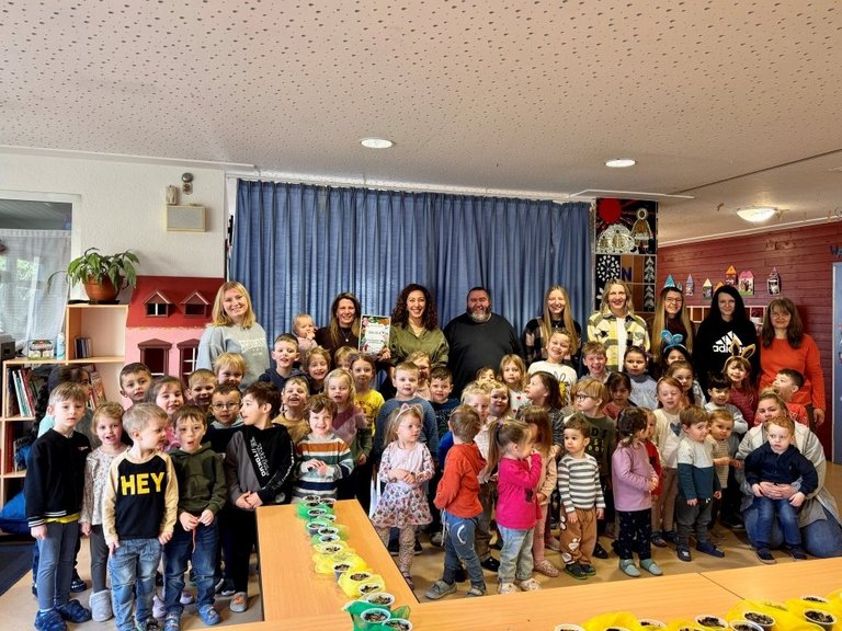 Auf dem Gruppenbild sind viele kleine Kinder in einem Kindergarten zu sehen. Dabei sind 10 Erwachsene.