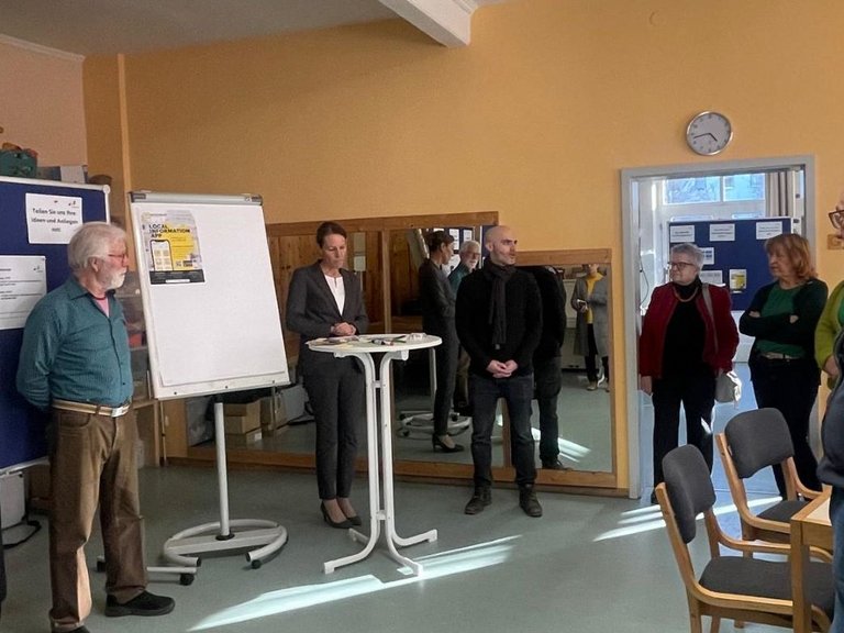 Auf dem Bild sind sechs Personen zu sehen, die im Kreis in einem Raum mit Pinnwänden stehen.