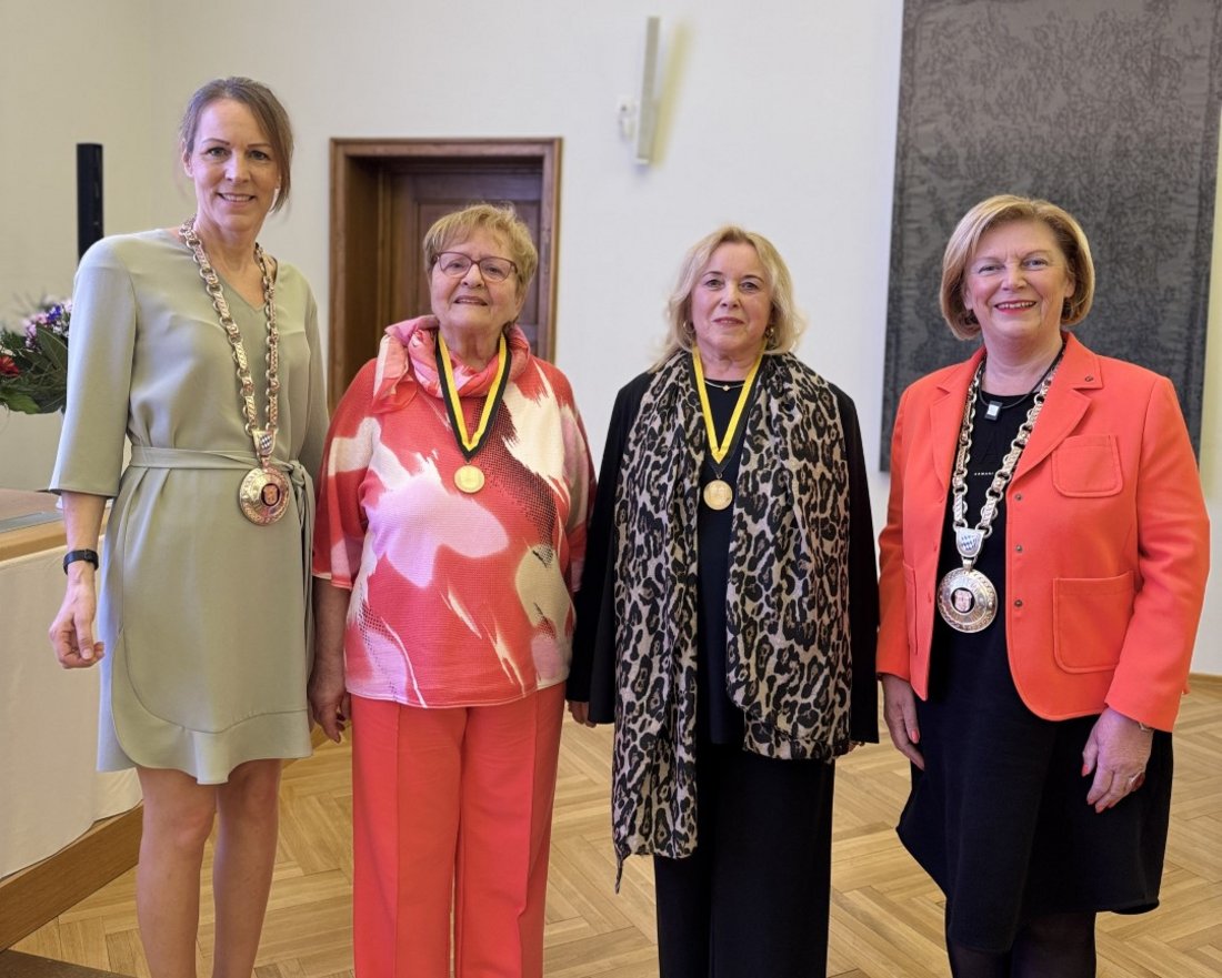 Auf dem Bild sind vier Frauen im Großen Sitzungssaal zu sehen. Die beiden äußeren tragen Amtsketten, die in der Mitte Ehrenmedaillen.