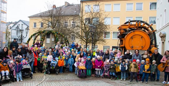 Many children and parents stand in front of the colorfully decorated Easter fountain.