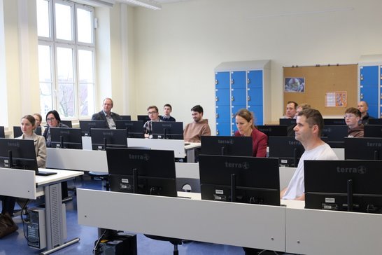 Auf dem Bild sind 13 Personen zu sehen, die an Computern sitzen.