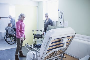 Auf dem Bild sind zwei Frauen zu sehen, die ein hochgeklapptes Bett anschauen.