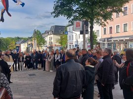 Auf dem Bild sind eine Menge Personen zu sehen, die auf einem Gehsteig im Halbkreis stehen.