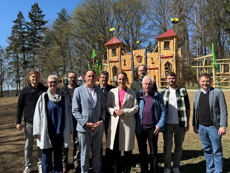 Auf dem Bild sind 10 Personen vor einer hölzernen Spielburg zu sehen.