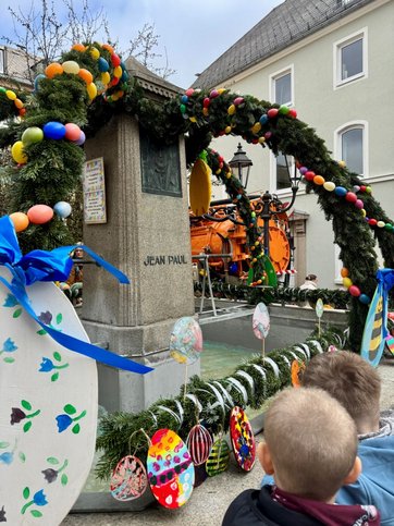 Auf dem Bild ist ein bunt geschmückter Brunnen mit der Aufschrift Jean Paul zu sehen.