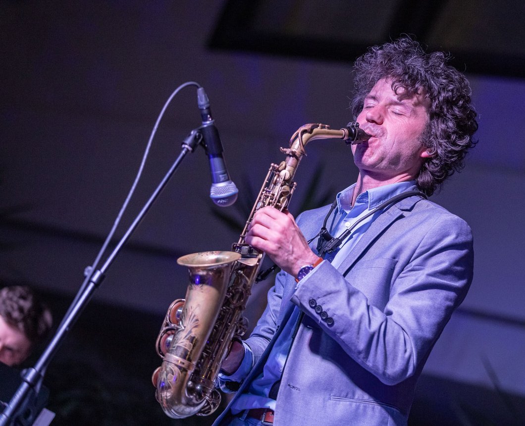 Auf dem Bild ist ein Mann zu sehen, der an einem Mikrofon Saxofon spielt.