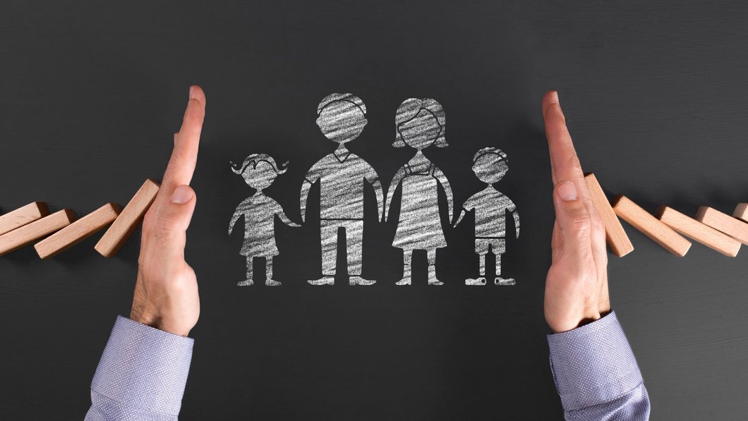 Zwei Hände halten schützend eine aufgezeichnete Familie mit zwei Kindern.