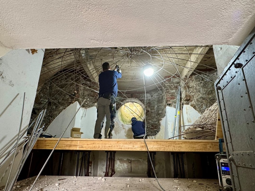 Auf dem Bild ist ein verfallenes Turmgewölbe zu sehen, an dem zwei Bauarbeiter arbeiten.