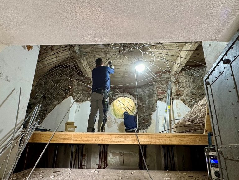 Auf dem Bild ist ein verfallenes Turmgewölbe zu sehen, an dem zwei Bauarbeiter arbeiten.