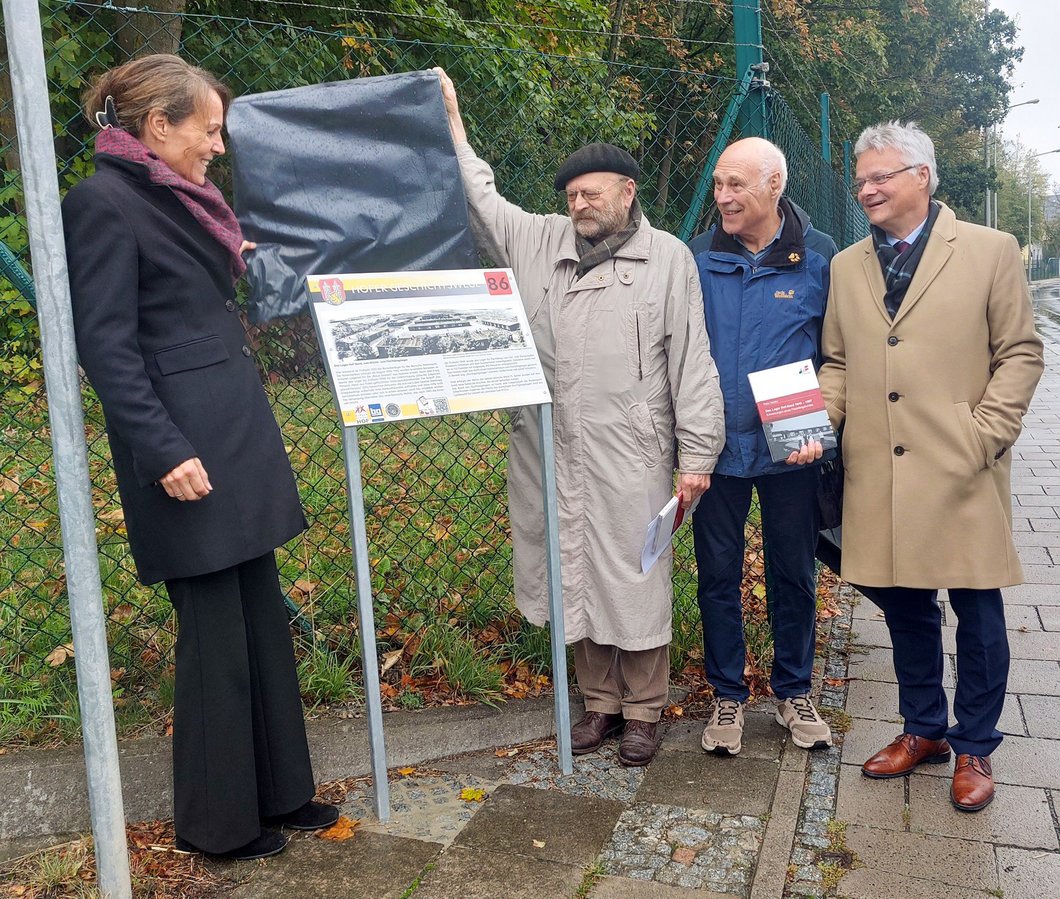 Auf dem Bild sind vier Personen zu sehen. Zwei von ihnen enthüllen eine Info-Tafel.