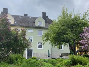 Auf dem Bild ist ein dreistöckiges Haus mit hellgrüner Fassade und Garten zu sehen.