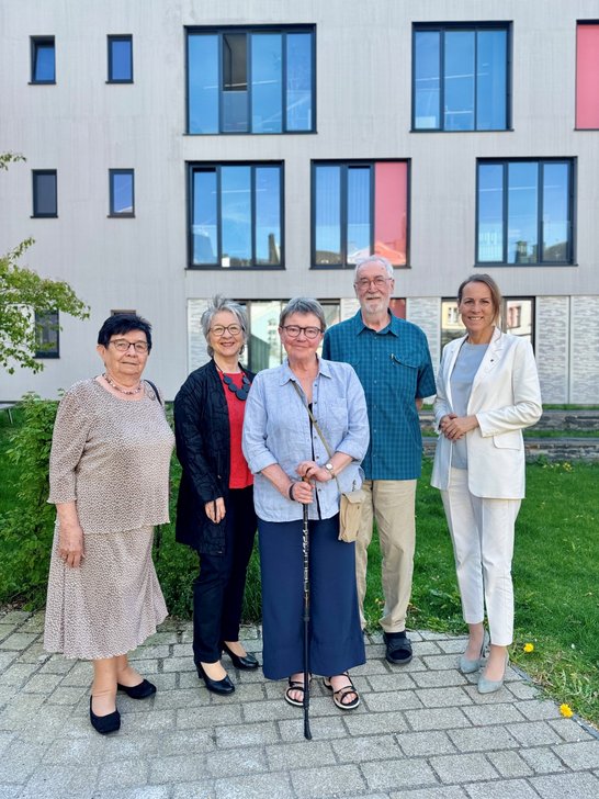 Auf dem Foto sind fünf Personen zu sehen, die vor einem modernen Gebäude stehen.