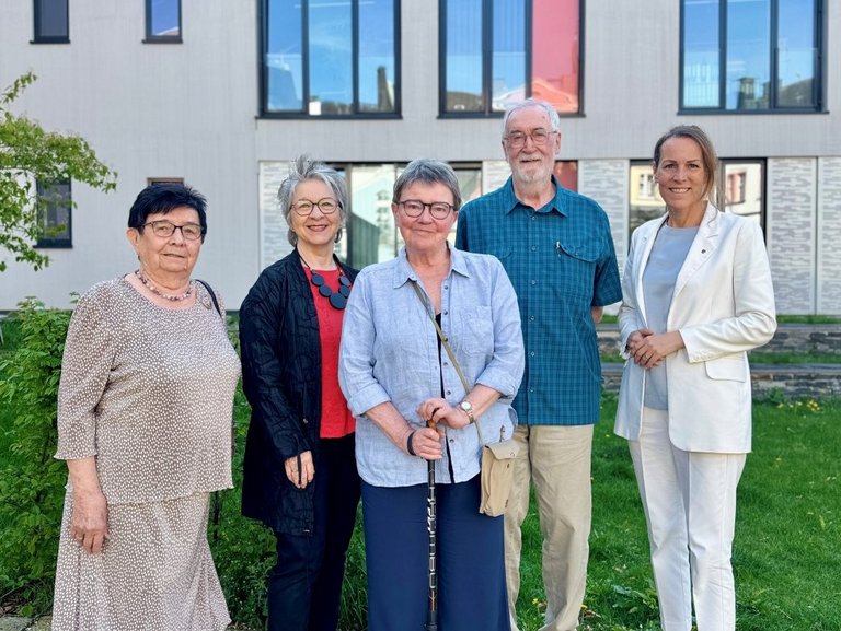 Auf dem Foto sind fünf Personen zu sehen, die vor einem modernen Gebäude stehen.