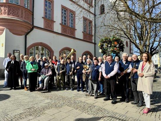 Auf dem Bild sind eine Menge Menschen zu sehen, die sich vor einem bunt geschmückten Brunnen aufgestellt haben.