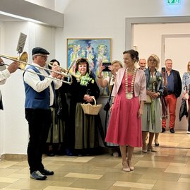 Auf dem Foto spielt ein Mann Trompete, mehrere Frauen und Männer hören zu.
