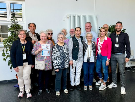 Auf dem Bild sind 13 Menschen zu sehen, die meisten davon sind alt.