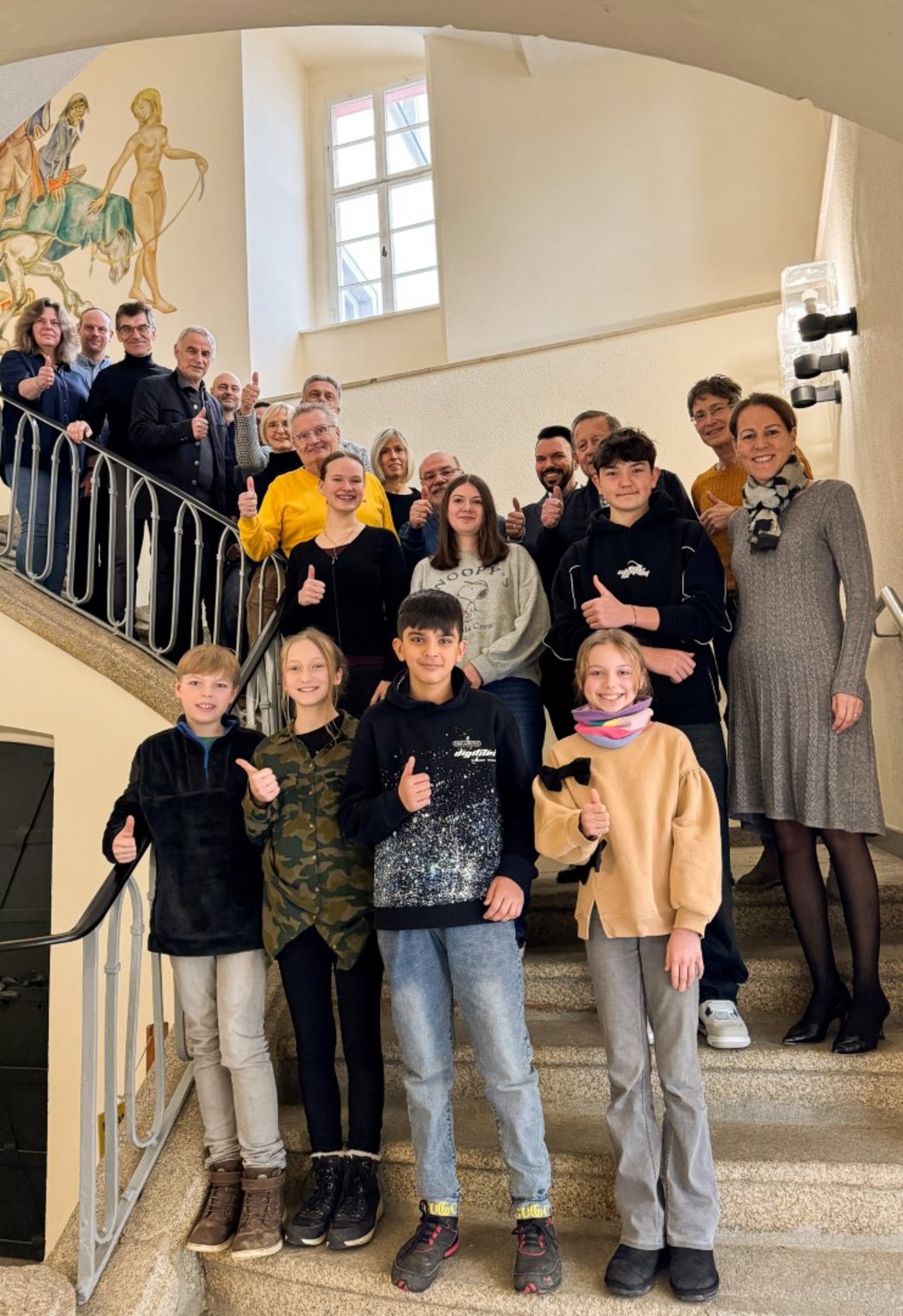 Auf dem Bild sind Kinder und Erwachsene zu sehen, die auf einer Treppe im Rathaus stehen und den Daumen nach oben halten.