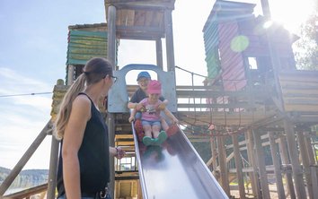 Auf diesem Foto ist ein Kind mit den Eltern auf dem Spielplatz