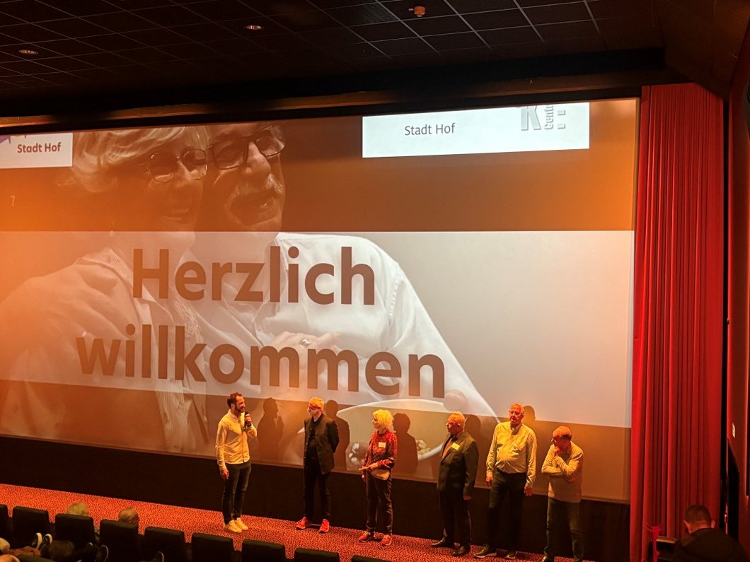 Auf dem Bild sind sechs Personen zu sehen, die vor einer Kinoleinwand stehen.