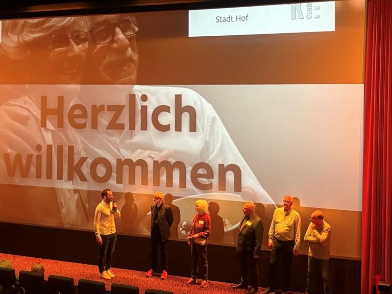 Auf dem Bild sind sechs Personen zu sehen, die vor einer Kinoleinwand stehen.