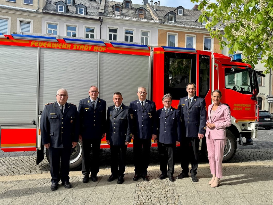 Auf dem Bild sind sechs Feuerwehrmänner in Uniform und eine Frau vor einem Feuerwehrfahrzeug zu sehen.