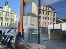 Auf dem Bild ist das Schaufenster eines Gebäudes von außen zu sehen, davor Baugeräte und Paletten.