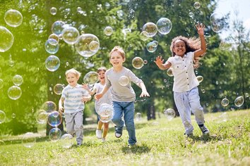 Das Bild zeigt vier Kinder die im Grünen mit Seifenblasen spielen.