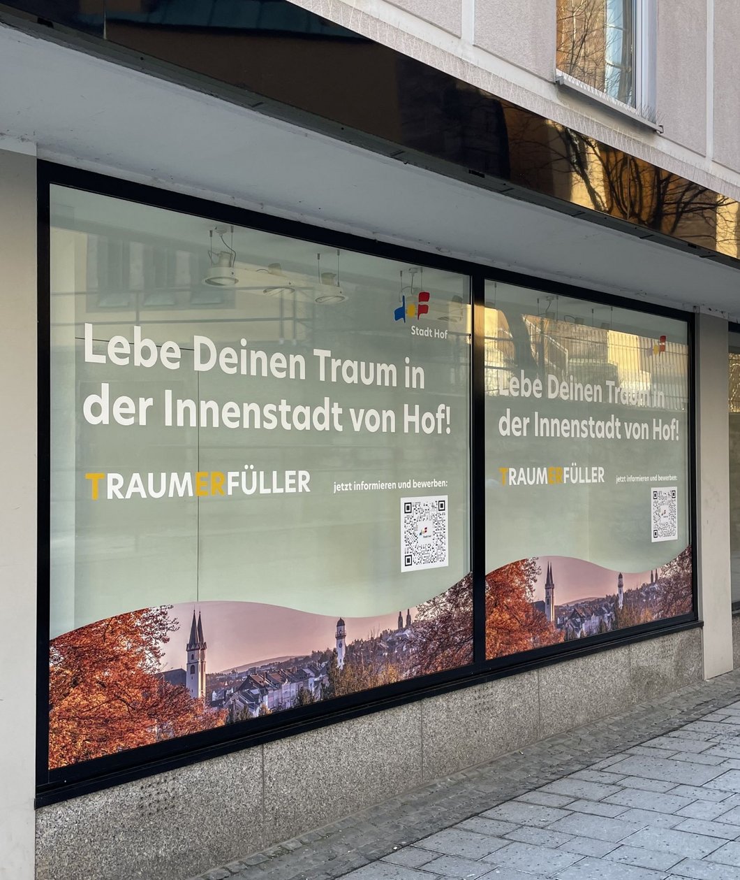 Das Bild zeigt ein Schaufenster, das mit einem Bild von Hof und der Aufschrift "Lebe Deinen Traum in der Innenstadt von Hof" beklebt ist.