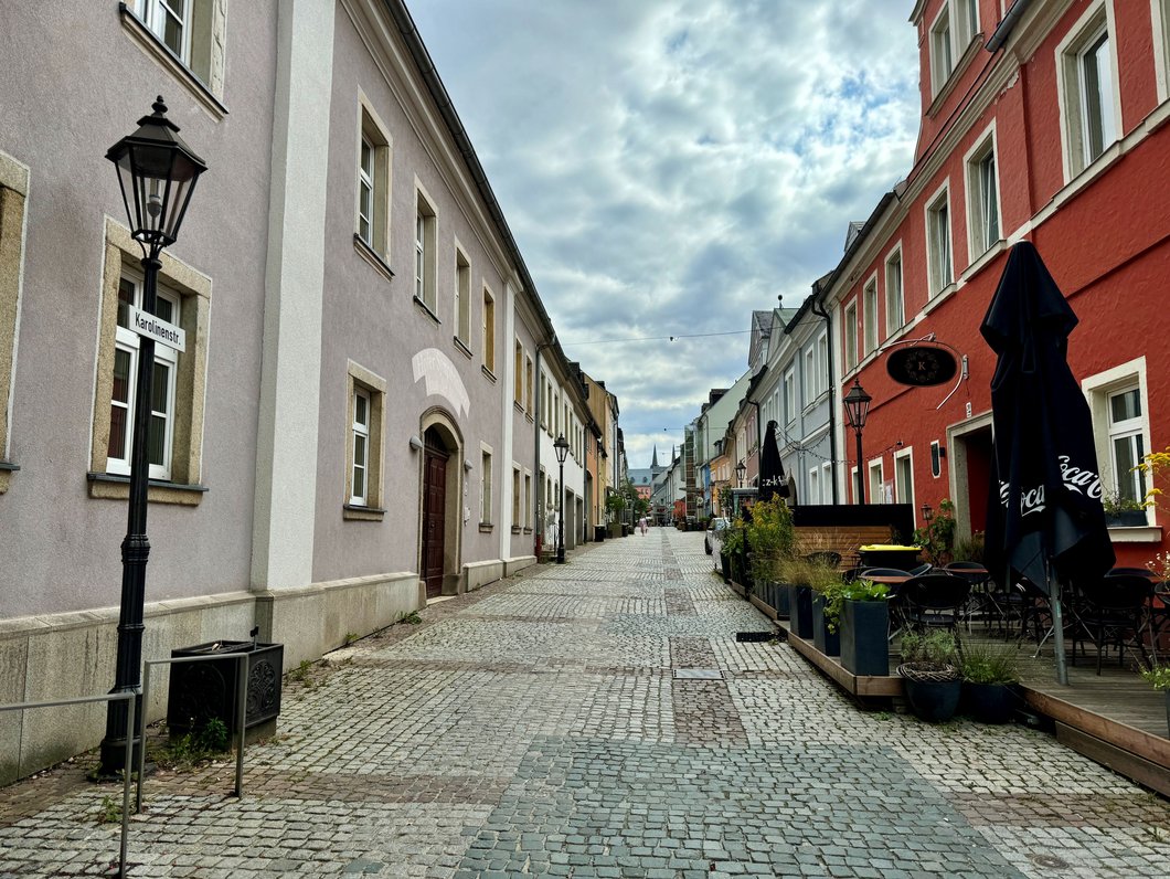 Auf diesem Bild ist eine gepflasterte Straße zu sehen, die von Gebäuden gesäumt ist. Auf einem Schild steht Karolinenstraße.
