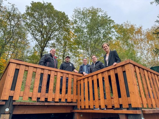 Auf dem Bild sind fünf Personen zu sehen, die am Geländer einer Holzterrasse stehen.