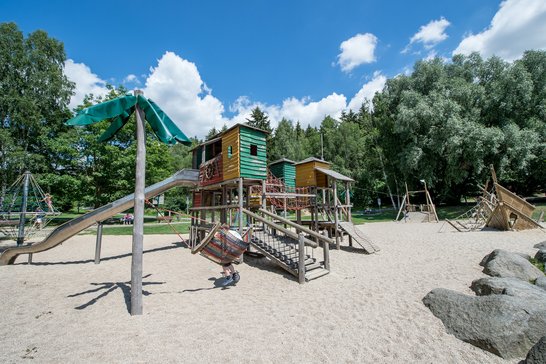 Auf dem Bild ist ein großer Spielturm auf einem Sandplatz zu sehen.