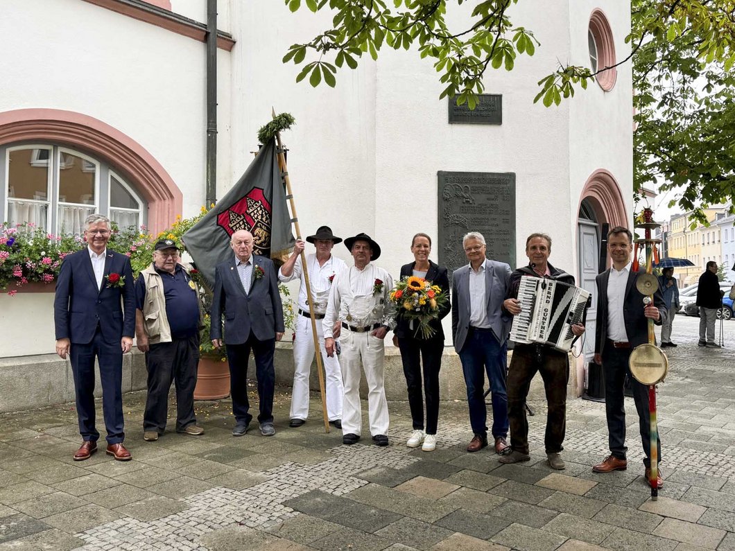 Auf dem Bild sind neun Personen zu sehen, davon zwei Handwerker in traditioneller Kleidung mit Fahne.