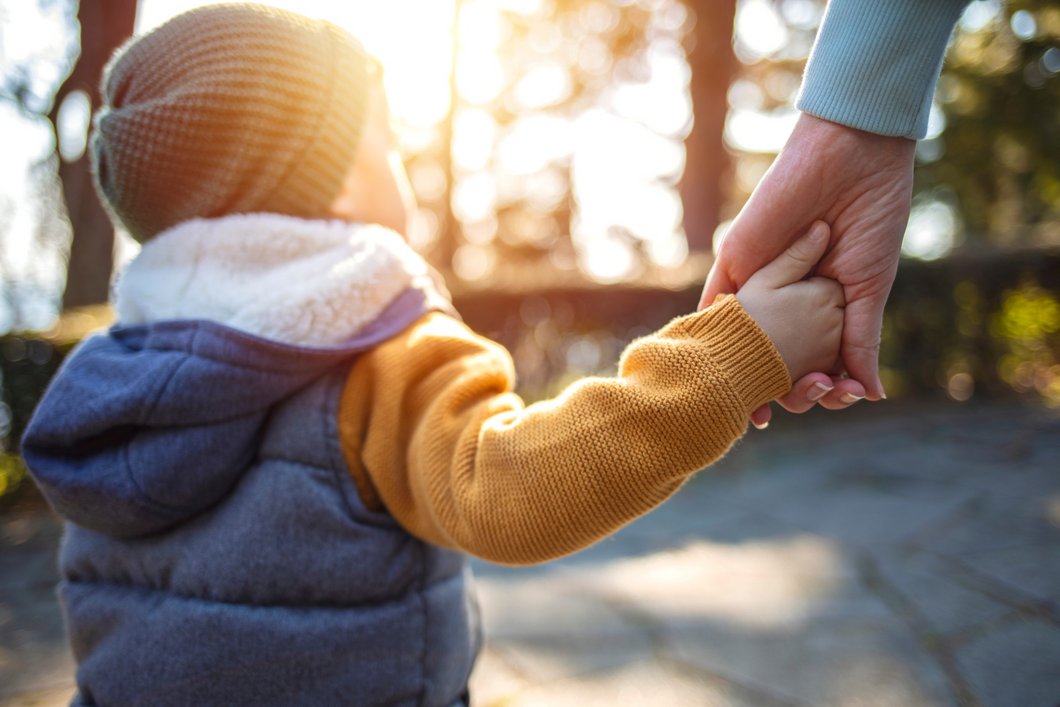 Das Bild zeigt ein kleines Kind, das die Hand einer erwachsenen Person hält.