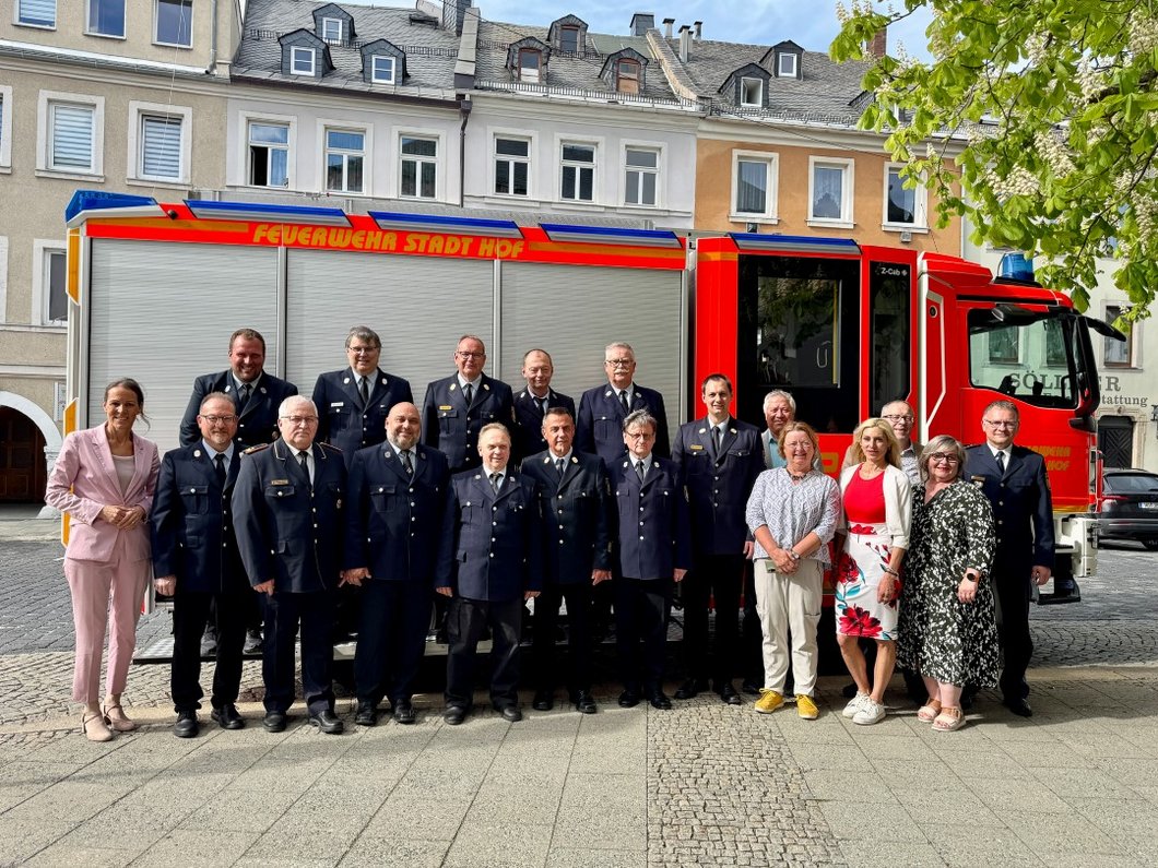 Auf dem Bild sind zwölf Feuerwehrmänner in Uniform und sieben weitere Personen vor einem Feuerwehrfahrzeug zu sehen.