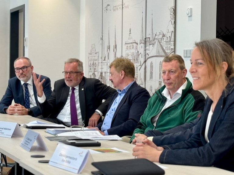 Auf dem Bild sind fünf Personen zu sehen, die nebeneinander an Sitzungstischen sitzen.