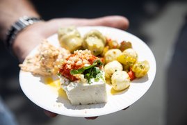 Auf dem Bild ist ein Teller mit schön angerichteten Antipasti zu sehen, gehalten von einer Männerhand.