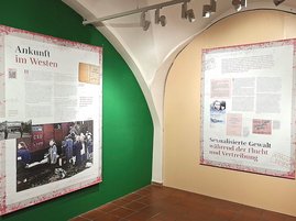 Das Bild zeigt Ausstellungsplakate zur Ankunft im Westen und sexualisierter Gewalt während der Flucht. 