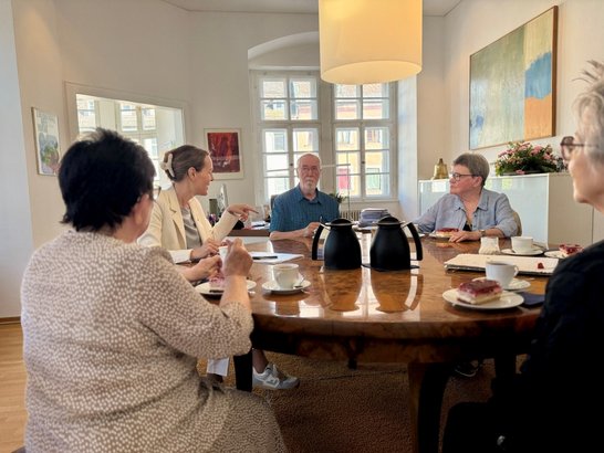 Auf dem Bild sind fünf Personen zu sehen, die an einer Kaffeetafel sitzen.