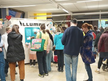 Auf dem Bild sind circa 20 Menschen zu sehen, jung und alt, die im Foyer der Stadtbücherei stehen.