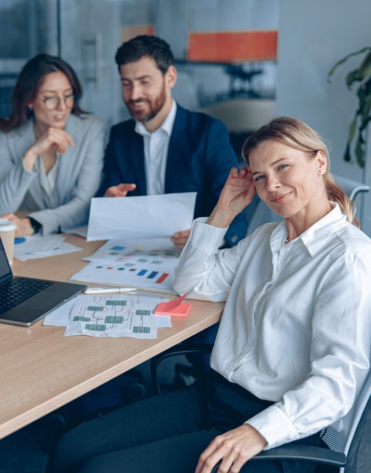 Auf dem Bild sind zwei Frauen und ein Mann zu sehen, die an einem Bürotisch sitzen.