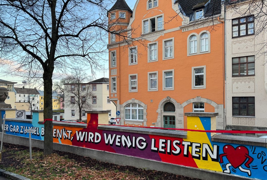 Auf dem Bild ist eine bunt bemalte, niedrige Mauer zu sehen, mit dem Spruch: "Wer gar zu viel bedenkt, wird wenig leisten"
