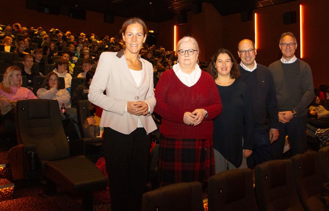 Auf dem Bild sind fünf Personen zu sehen, die in einem Kino stehen, hinter ihnen das Publikum.