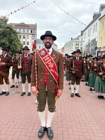 Auf dem Bild ist eine Trachtenkapelle in einer geschmückten Straße zu sehen.