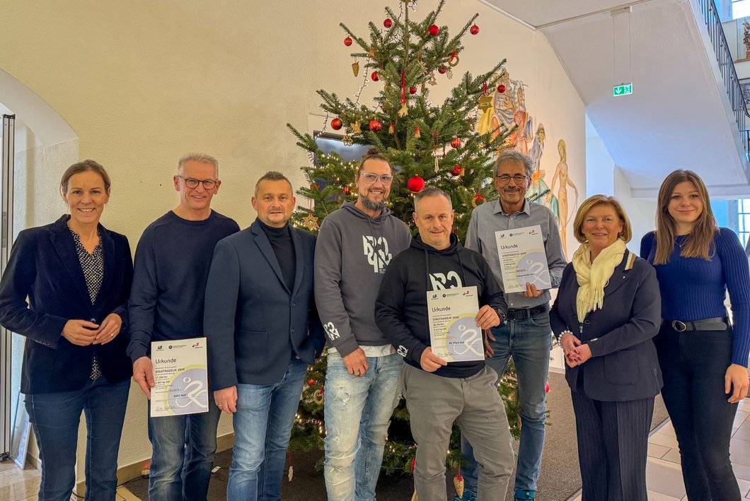 Auf dem Bild sind acht Personen zu sehen, drei von ihnen halten Urkunden.