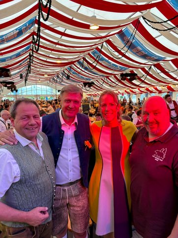 Auf dem Bild sind drei Männer und eine Frau in einem Festzelt zu sehen.