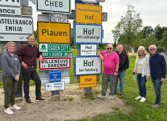 Auf dem Bild sind sechs Personen zu sehen, die neben vielen Ortsschildern stehen.