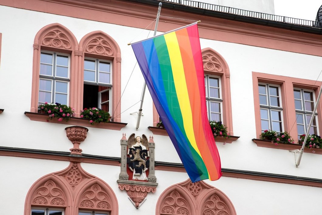 Auf dem Bild ist eine Regenbogenfahne zu sehen, die an der Fassade des Hofer Rathauses hängt.