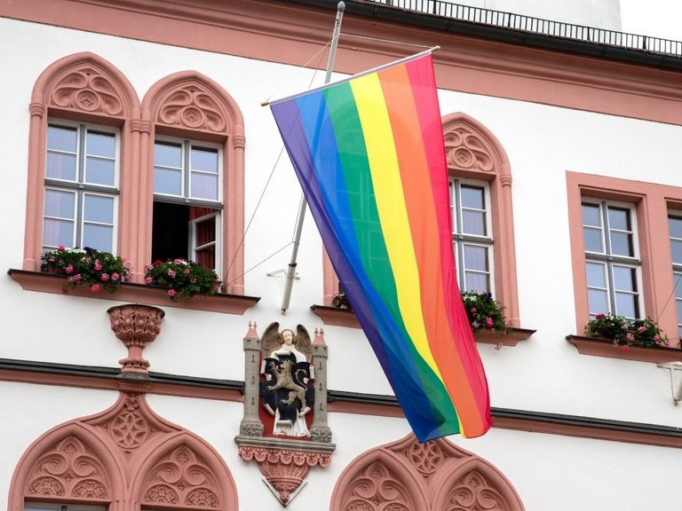 Auf dem Bild ist eine Regenbogenfahne zu sehen, die an der Fassade des Hofer Rathauses hängt.