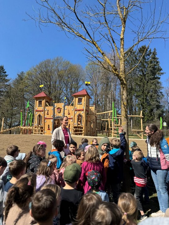 Auf dem Bild sind zwei Frauen mit einer Schar Kinder zu sehen, im Hintergrund eine hölzerne Spielburg.